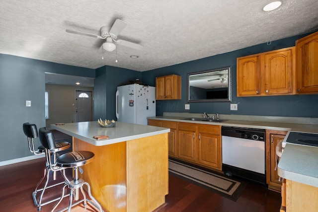 kitchen with a center island, dark wood-type flooring, white appliances, a ceiling fan, and a sink