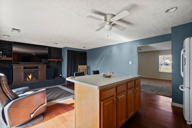 kitchen featuring a ceiling fan, wood finished floors, open floor plan, freestanding refrigerator, and a fireplace