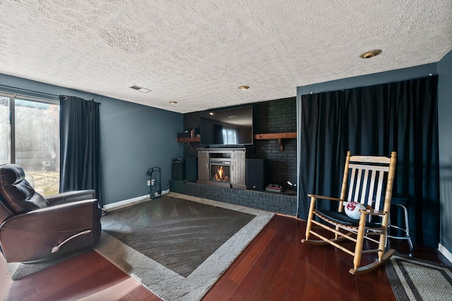 living area with wood finished floors, visible vents, baseboards, a textured ceiling, and a brick fireplace