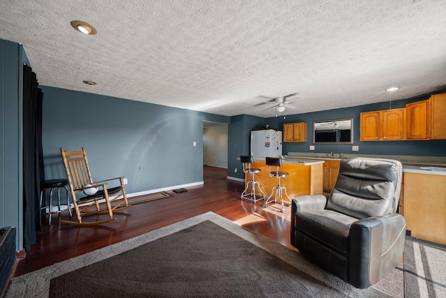 living room with a ceiling fan, wood finished floors, baseboards, a textured ceiling, and indoor bar