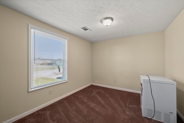 empty room with visible vents, baseboards, a textured ceiling, and dark carpet