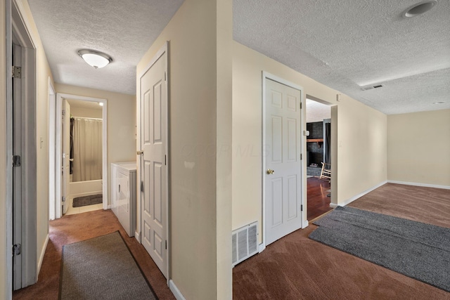 hallway featuring visible vents, baseboards, carpet, washing machine and dryer, and a textured ceiling