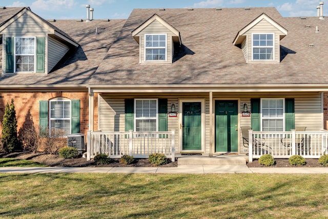 cape cod house featuring a front yard, brick siding, covered porch, and roof with shingles