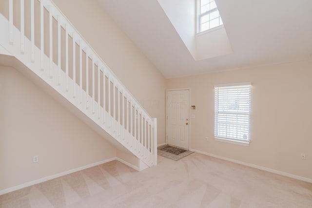 carpeted foyer entrance with stairway, vaulted ceiling with skylight, and baseboards