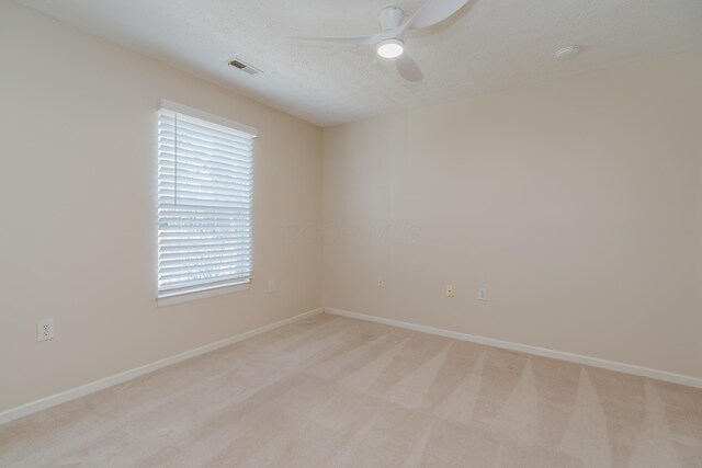 empty room featuring visible vents, baseboards, light colored carpet, a textured ceiling, and a ceiling fan