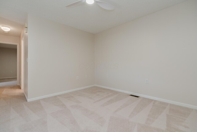 spare room with visible vents, baseboards, light colored carpet, and a ceiling fan