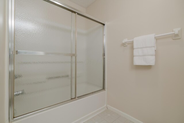 bathroom featuring baseboards and bath / shower combo with glass door