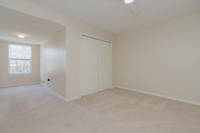 unfurnished bedroom featuring light carpet, a textured ceiling, a closet, baseboards, and ceiling fan