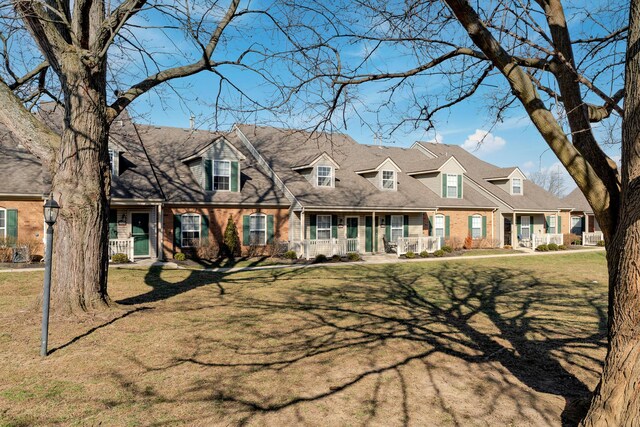 cape cod-style house with a front yard, covered porch, brick siding, and a residential view