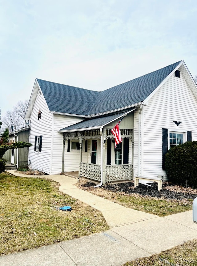 view of front facade with a front lawn, covered porch, and a shingled roof