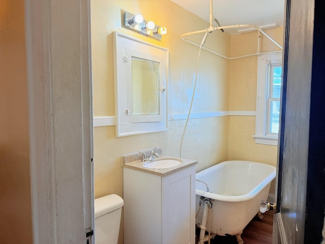 full bath with tile walls, toilet, wood finished floors, a soaking tub, and vanity