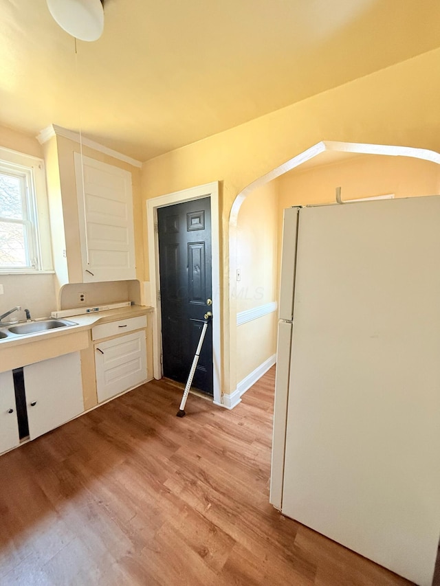 kitchen featuring light countertops, freestanding refrigerator, light wood-style floors, white cabinets, and a sink