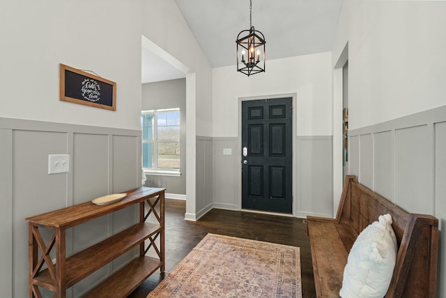 entryway with dark wood finished floors, a wainscoted wall, lofted ceiling, and an inviting chandelier