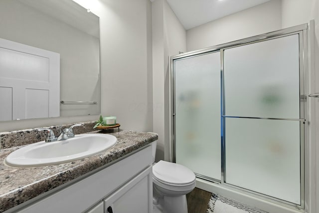 bathroom featuring vanity, toilet, wood finished floors, and a stall shower