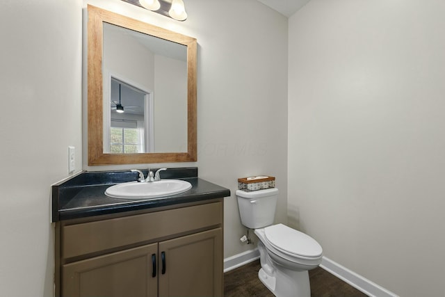 half bath with baseboards, toilet, wood finished floors, and vanity