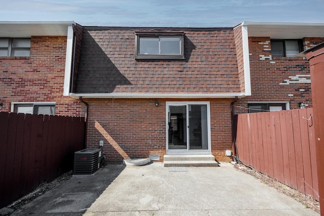 back of house with cooling unit, brick siding, and roof with shingles