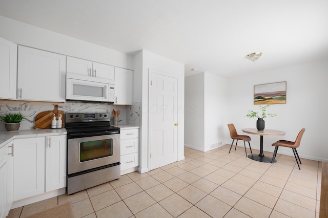 kitchen with light tile patterned floors, white microwave, electric range, white cabinetry, and tasteful backsplash