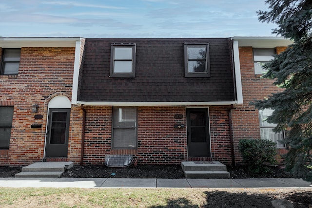 view of front of house featuring mansard roof, brick siding, and a shingled roof