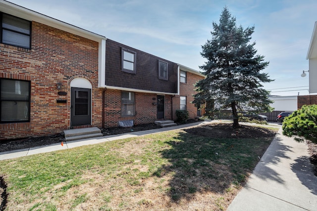 view of front of home with brick siding, a shingled roof, and a front yard