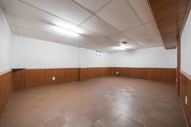 empty room with visible vents, wood walls, light floors, wainscoting, and a paneled ceiling