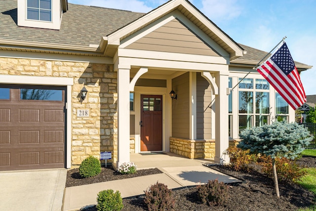 doorway to property with a garage, stone siding, driveway, and a shingled roof