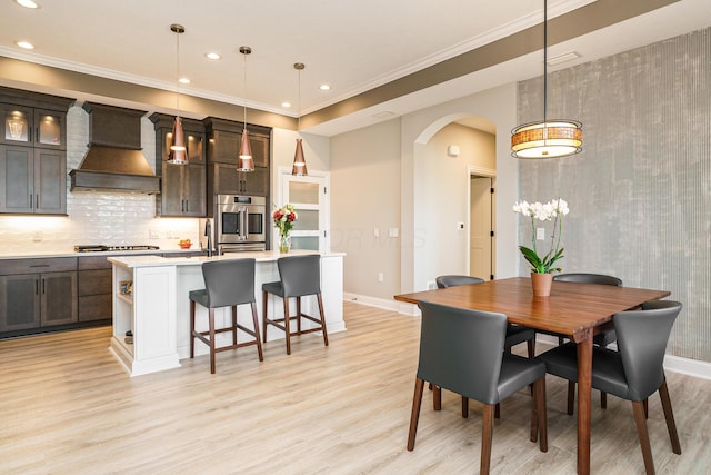 dining room featuring baseboards, recessed lighting, arched walkways, ornamental molding, and light wood-type flooring