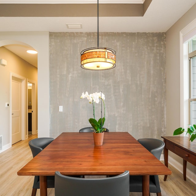 dining space featuring an accent wall, light wood-style flooring, baseboards, and arched walkways