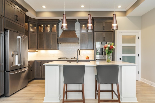 kitchen featuring premium range hood, a sink, stainless steel appliances, dark brown cabinetry, and light countertops