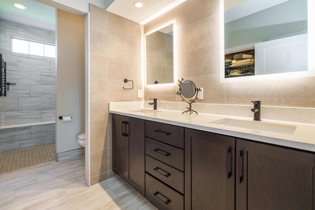 full bathroom with double vanity, toilet, tile walls, and a sink