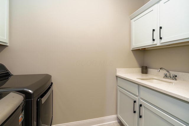 clothes washing area featuring washing machine and dryer, cabinet space, baseboards, and a sink