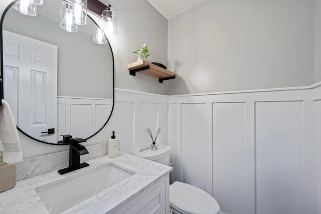 half bath with a wainscoted wall, toilet, and vanity