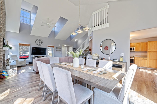 dining room with stairway, ceiling fan with notable chandelier, light wood-style floors, and a towering ceiling