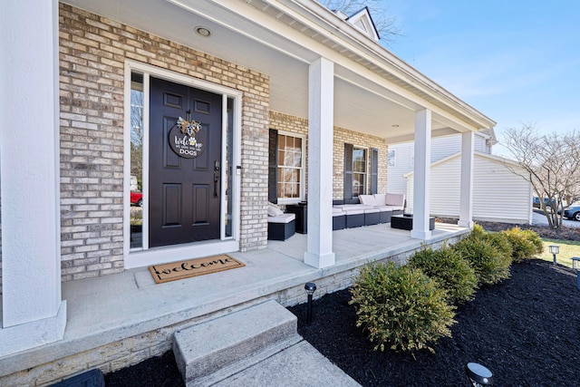 view of exterior entry featuring brick siding, an outdoor living space, and covered porch