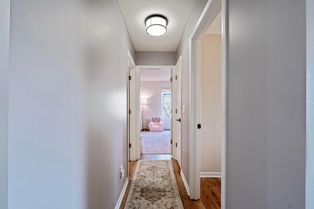 hall with a textured ceiling, baseboards, and wood finished floors