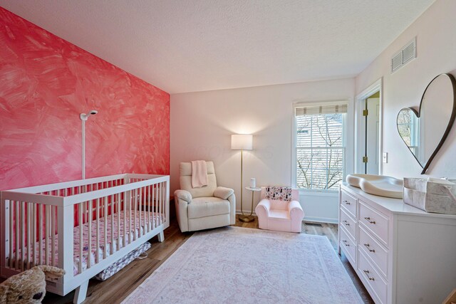 bedroom with visible vents, a crib, a textured ceiling, and wood finished floors