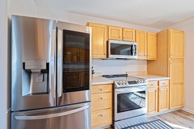 kitchen with light brown cabinets, light wood-style flooring, light countertops, appliances with stainless steel finishes, and a textured ceiling