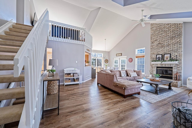 living room with stairway, a fireplace, wood finished floors, and a ceiling fan