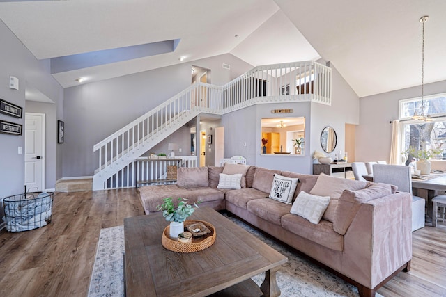 living room with stairway, wood finished floors, baseboards, high vaulted ceiling, and a notable chandelier