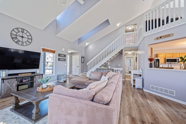 living area with wood finished floors, baseboards, visible vents, high vaulted ceiling, and stairs