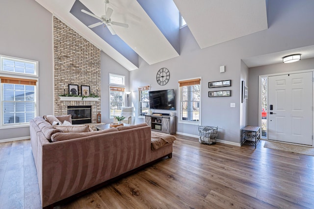 living room with a brick fireplace, baseboards, ceiling fan, wood finished floors, and high vaulted ceiling