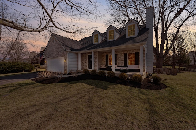 cape cod home featuring driveway, a porch, an attached garage, a lawn, and brick siding