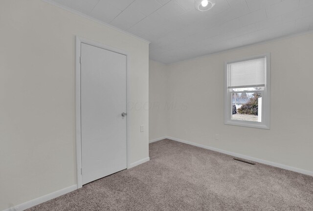 carpeted spare room featuring visible vents, baseboards, and ornamental molding