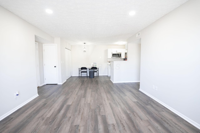 unfurnished living room featuring visible vents, a textured ceiling, dark wood-type flooring, and baseboards