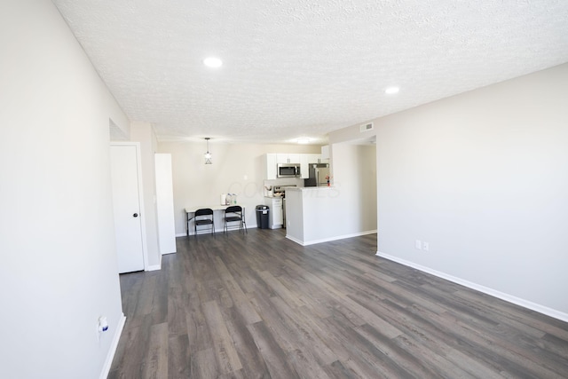 unfurnished living room with dark wood finished floors, visible vents, a textured ceiling, and baseboards