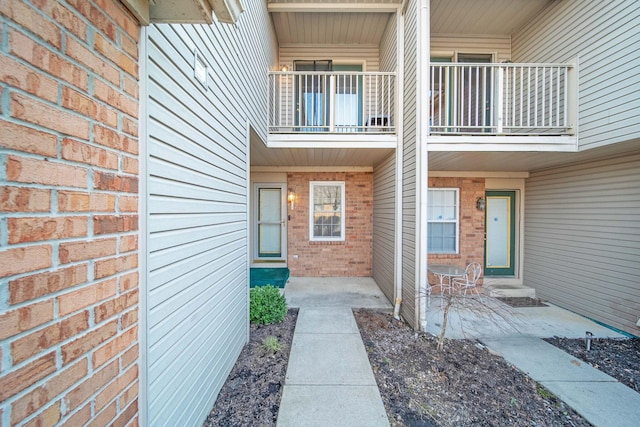 view of exterior entry with a balcony and brick siding