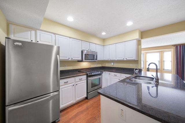 kitchen featuring a sink, wood finished floors, white cabinetry, dark stone counters, and appliances with stainless steel finishes