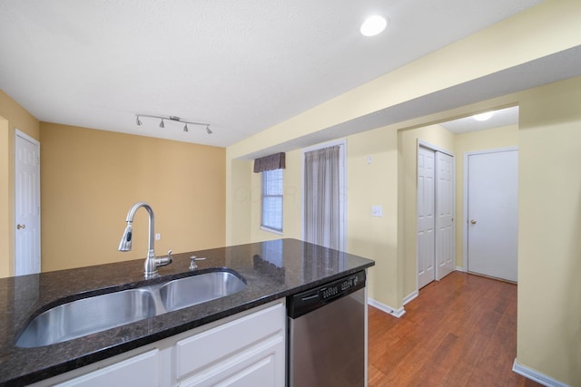 kitchen with dishwasher, dark stone countertops, dark wood-style floors, white cabinets, and a sink