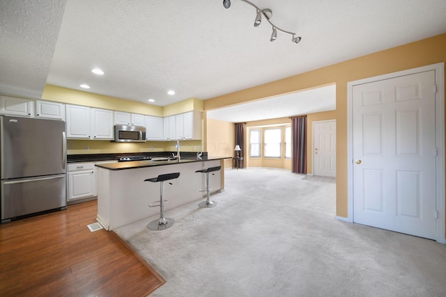 kitchen featuring dark countertops, a breakfast bar area, white cabinets, stainless steel appliances, and a sink