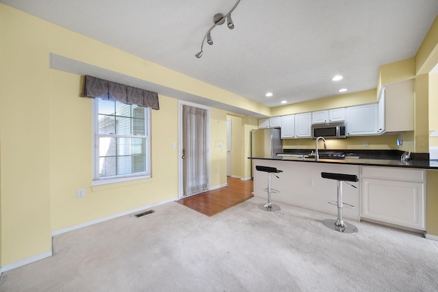 kitchen featuring visible vents, dark countertops, stainless steel appliances, a breakfast bar area, and light colored carpet