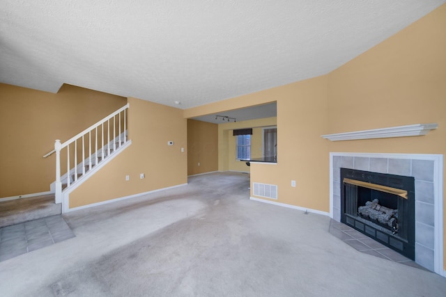 unfurnished living room with visible vents, a textured ceiling, a fireplace, baseboards, and stairs